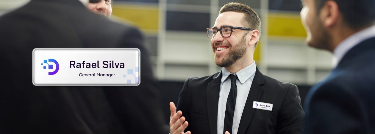 Business professionals in suits engaging in a discussion, one with a business name tag.
