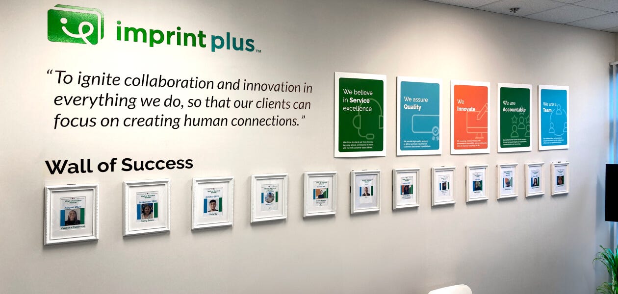 A photo of the ImprintPlus Wall of Success showcasing various achievements and awards in a professional setting.