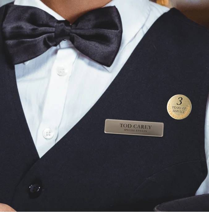 A professional waiter in a black vest and bow tie wearing a name badge and lapel pin